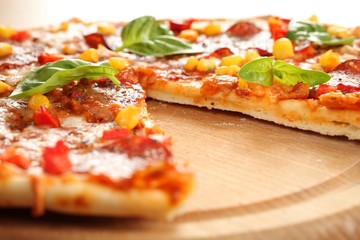Pizza with salami, corn and herbs on wooden tray.