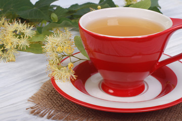 Herbal tea with lime in a red cup on a wooden table.