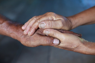 Hand of an elderly woman holding the hand of an elderly man.