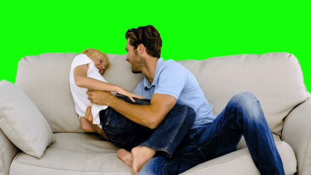 Father tickling son on the sofa on green screen