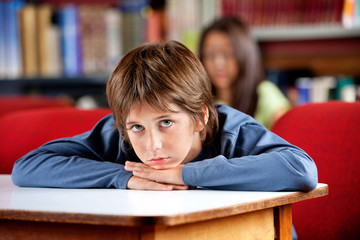 Portrait Of Bored Schoolboy Leaning On Table In Library