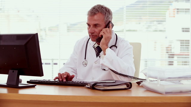 Doctor picking up the phone and using his computer