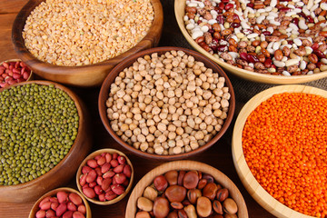 Different kinds of beans in bowls on wooden background