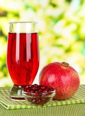 Glass of fresh garnet juice on table on bright background