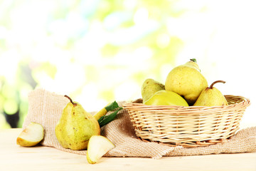Pears in basket on burlap on wooden table on nature background