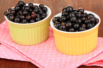Fresh black currant in bowls on napkin on wooden background