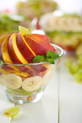 Tasty fruit salad in glass bowl, on white wooden table