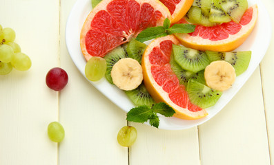 Assortment of sliced fruits on plate, on white wooden table