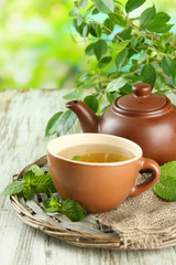 Teapot and cup of herbal tea with fresh mint on wooden table