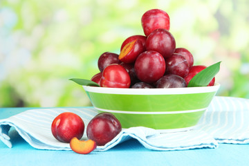 Ripe plums in bowl on wooden table on natural background