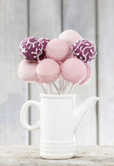 Pink and purple cake pops in white ceramic jug on wooden back