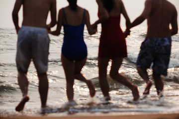 Fototapeta na wymiar Four friends running into the water on a sandy beach, Silhouette