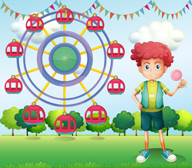 A boy holding a lollipop beside a ferris wheel