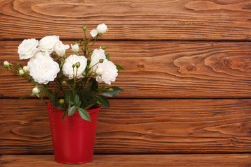 White roses in a red bucket on a wooden background