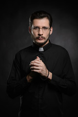 Praying priest. Portrait of priest standing isolated on black