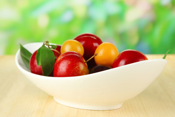 Ripe plums in plate on wooden table on natural background