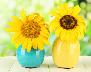 Bright sunflowers in vase on wooden table on natural background