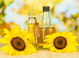 Oil in jars and sunflower on wooden table close-up