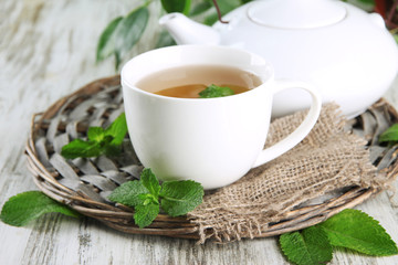 Teapot and cup of herbal tea with fresh mint on wooden table