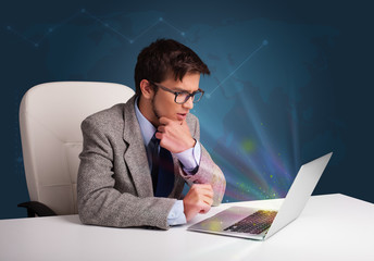 Handsome man sitting at desk and typing on laptop with abstract