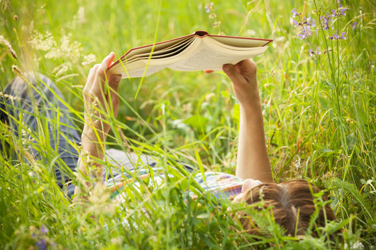 girl reading a book lying in the tall grass