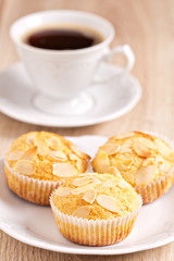 Three muffins with almonds on a plate and a cup of coffee