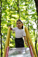 The kid climbed the slide on blurred background of trees