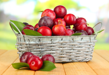 Ripe plums in basket on wooden table on natural background