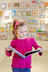 Little girl stands reading open book in book department at store