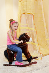Little girl rocks on hobbyhorse in play room © Pavel Losevsky