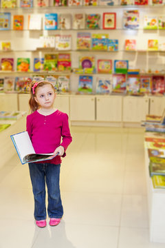 Little girl stands looking thoughtful holding open book