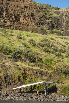 people carrying hang glider up steep slope