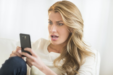 Fototapeta premium Amazed Woman Looking At Mobile Phone On Sofa