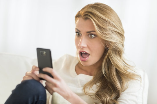 Shocked Woman Looking At Mobile Phone At Home