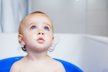 Baby girl sitting in bathtub looking up