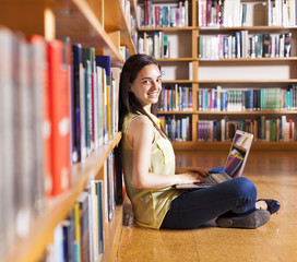 Portrait of a young smiling student using her laptop in a librar
