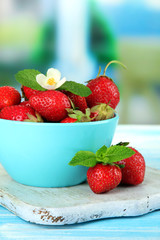 Ripe sweet strawberries in bowl on blue wooden table