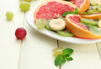 Assortment of sliced fruits on plate, on white wooden table