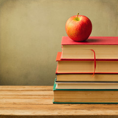 Old books and apple on wooden table over grunge background