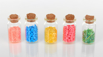 Different colorful beads in bottles isolated on white