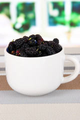 Fototapeta na wymiar Ripe mulberries in cup on table in room