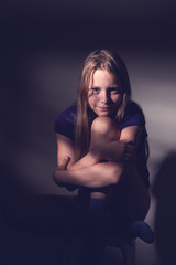 Portrait of a teen girl sitting on a chair in a dark room, contr