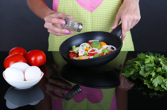 Hands cooking vegetable ragout in pan on gray background