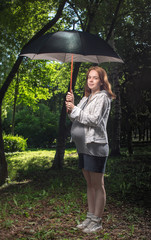 The pregnant woman costs in park under a umbrella