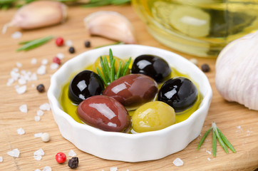 bowl with different olives in olive oil and spices on a wood