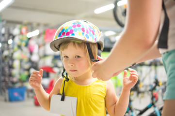 Adorable girl fitting bike helmet in sport store