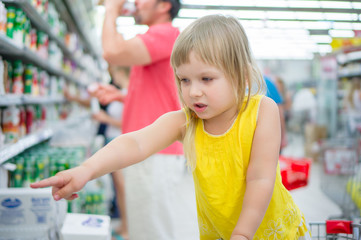 Adorable girl in shopping cart pointing hand to goods in superma