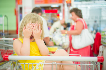 Adorable girl sit in shopping cart and close face with hands nea