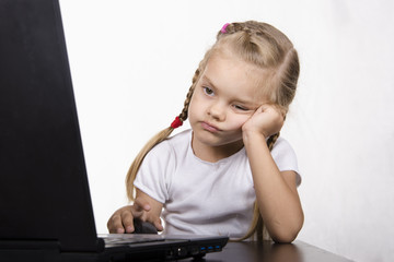 Девочка сидит за столом и работает за ноутбуком