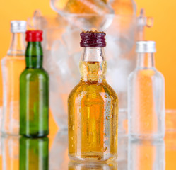 Minibar bottles in bucket with ice cubes,  on color background